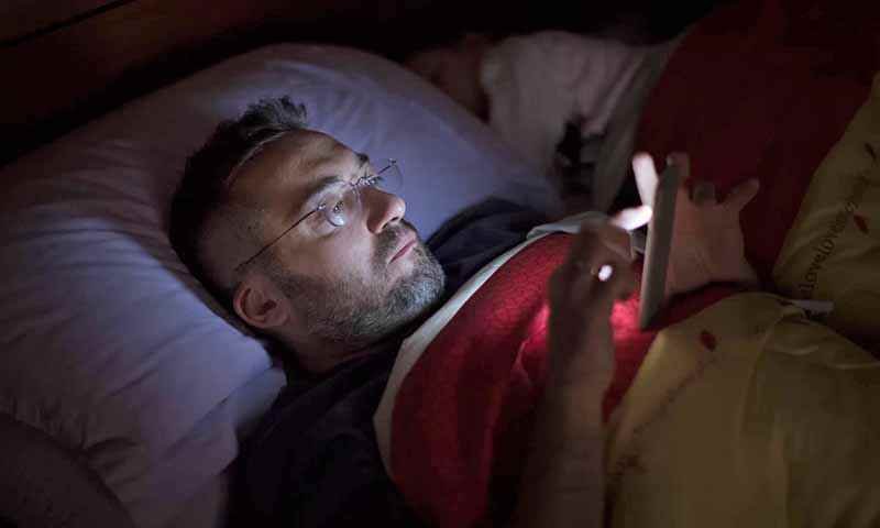 Un hombre lee a oscuras con su smartphone en la cama. GETTY IMAGES